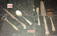 Full view of all eight pieces including the sterling handled rug hooking tool and seven serving utensils on dark cloth background.