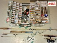 Full view of tackle box with multiple trays displaying an assortment of vintage fishing lures, alongside two fishing rods laid out on the floor.
