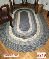 Oval braided rug on a hardwood floor with part of a wooden chair and table visible, showing the pattern and condition.