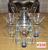 Front facing photo of vintage cocktail set showing six glasses with colored bases surrounding metal shaker in carrier