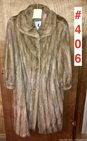 Front view of vintage full-length mink coat hanging on a wooden door, showing the coat's shawl collar, covered button fronts, and full sleeves.
