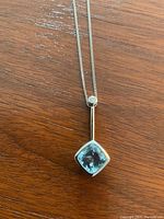 Close-up showing square-cut aquamarine set in white gold pendant with a smaller white gemstone near the chain loop.