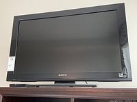 Front view of Sony 32 inch TV with black glossy bezel and stand, Sony logo on bottom center, model sticker on lower right corner.