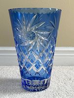 Close-up of blue crystal vase showing detailed cut glass with diamond and starburst patterns, scalloped rim visible.
