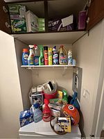 Lower shelf with boxed and grouped cleaning supplies including wipes, detergents, insect repellent, toilet paper, and cleaning cloths