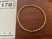 Top down view of twisted gold filled bangle bracelet on wood surface next to a measurement paper showing lot number.