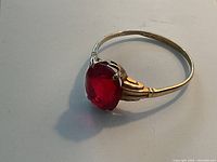 Close-up view of the ring showcasing the oval red glass stone and gold band details.