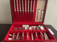Full view of the open red storage case displaying all silverware pieces neatly arranged including knives in lid and spoon/fork sets in the base compartments.