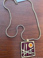 Full view of the necklace showing the silver woven chain and rectangular enamel pendant.