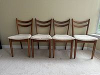 Front view of four teak dining chairs in a row against a wall on carpet