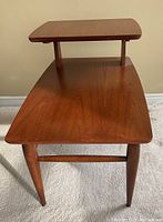 Front view showing the entire two-tier teak end table with tapered legs and warm wood grain finish.