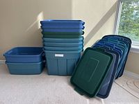 9 full size, 2 medium size and 1 small Rubbermaid storage bins stacked with lids leaning against wall