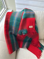 Scottish wool plaid throw blanket draped over a couch, showing bright red and green tartan with fringed edges.