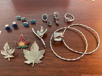 Full view of the sterling silver jewelry lot including rings, bangles, earrings, and maple leaf brooches arranged on a wooden surface.