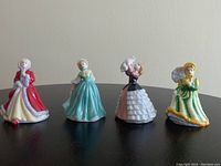 Front and side views of four tiny Royal Doulton porcelain figurines depicting women in period dresses of red, teal blue, black-pink, and green-yellow with accessories like a dove and parasol.