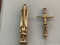 Front view of two gold totem pole charms on white background showing design details and loop bails