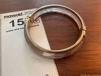 Photo of the vintage Italian molded glass and gold tone hinged bangle bracelet resting on paper next to a maxsold lot number card.