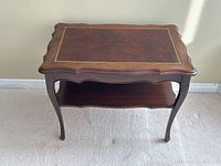 Top down view of vintage end table showing hand tooled leather top with decorative gold trim and solid walnut scalloped edges