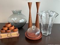 Photo showing all items in the lot including two teak candle holders, colored glass vase, clear glass vase, teak and glass butter dish, and a set of teak napkin rings in box.