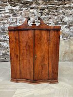 Front view of closed cabinet, showing overall shape, wood grain and pediment.