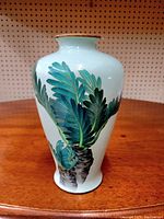 Front view of vase showing green and blue leafy decoration on white base.