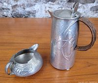 Full view of the tankard and creamer on wooden surface showing texture and design details