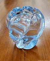 Clear organic art glass vase with fluid, flowing form and thick base showing slight bluish tint, on wooden surface.