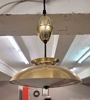 Side view of the brass dome-shaped pendant lamp showing dents and scratches on the shade surface and the pull mechanism above.