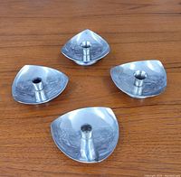 Four stainless steel mid century modern candle holders arranged on wood surface, showing triangular shapes with rounded corners and central candle sockets.