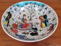 Interior view of the pottery bowl showing a detailed hand-painted scene with traditionally dressed figures sitting or standing around a central tree with floral motifs.