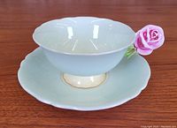 Front-angle view of tea cup on saucer showing overall shape, color, scalloped rims, rose handle detail