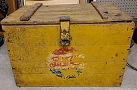 Front view of the wooden cooler showing yellow paint and a faded Pepsi logo on the front.