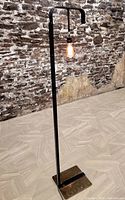 Floor lamp standing upright showing full height and base detail against stone wall.