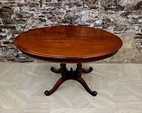 Full view of round wooden table showing the top surface and part of the pedestal legs against a stone wall background.