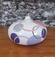 Side view of the vintage art pottery vase showing the oversized flattened bulbous shape with painted multi-colored overlapping circles in pink, purple, and lavender.