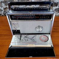 Front view showing tuning dial, volume, tone and AM/FM selector controls, with fold-down lid displaying printed world map and station logs charts