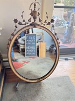 Full view of oval mirror showing gold painted ornate frame with beaded edge and decorative floral finial at top.
