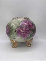 View of hand painted pink flowers and green leaves on round vase with gold feet showing artistic detailing and scalloped gold rim