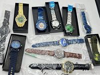 Overview photo of eleven men's/unisex watches in various styles and colors arranged side by side including metal link, leather-like, fabric, nylon straps.
