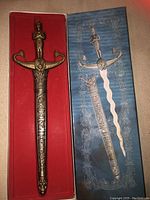 Miniature sword in sheath with box showing the detailed hilt and ornate blade.