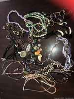 Top-down shot showing an assortment of colorful necklaces, bracelets, pins, and earrings laid out on a dark surface.