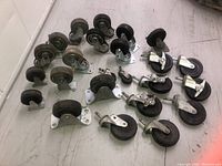 Photo showing a variety of caster wheels in different sizes and mounting types, placed on a light colored floor.