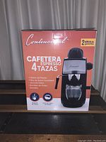 Image of the front side of the box showing the espresso maker and its features including 4 cups capacity, 5 bars of pressure, stainless steel filter, glass carafe, removable drip tray, and powerful steamer.