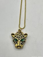 Front view of jaguar head pendant with gold-tone chain laid flat, showing emerald eyes and black rhinestone details.