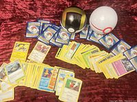 Spread of Pokemon cards laid out on a red surface showing both card front and backs with two Pokeball containers.