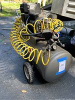 Front angle view of Campbell Hausfeld air compressor showing cylindrical tank, yellow coiled hose, handle, and wheels