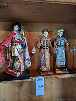 Photo showing all three dolls: Japanese Geisha on the left, and Chinese Emperor and Empress on the right on shelf