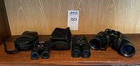 Three pairs of binoculars and their cases/pouches displayed on a wooden surface.