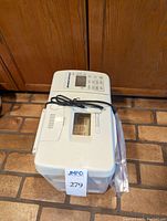 Full view of white Breadman Ultimate bread maker with power cord placed on brick floor.
