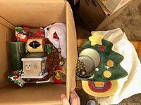 Open box showing ceramic tree-shaped dish and assorted vintage ornaments including a small building-shaped ornament and round baubles